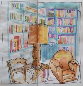 Au premier plan : fauteuil en cuir blond, grande lampe dans les mêmes teintes, chaise. A l'arrière plan, une bibliothèque peinte en bleue et remplie de livres.